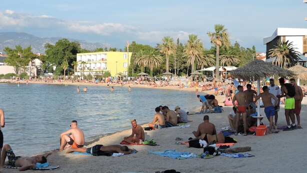 Una playa con gente tomando el sol y nadando.