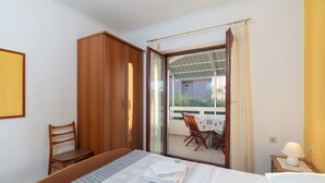 Habitación de hotel con cama, armario de madera, una silla, mesa con sillas afuera y balcón con vistas.