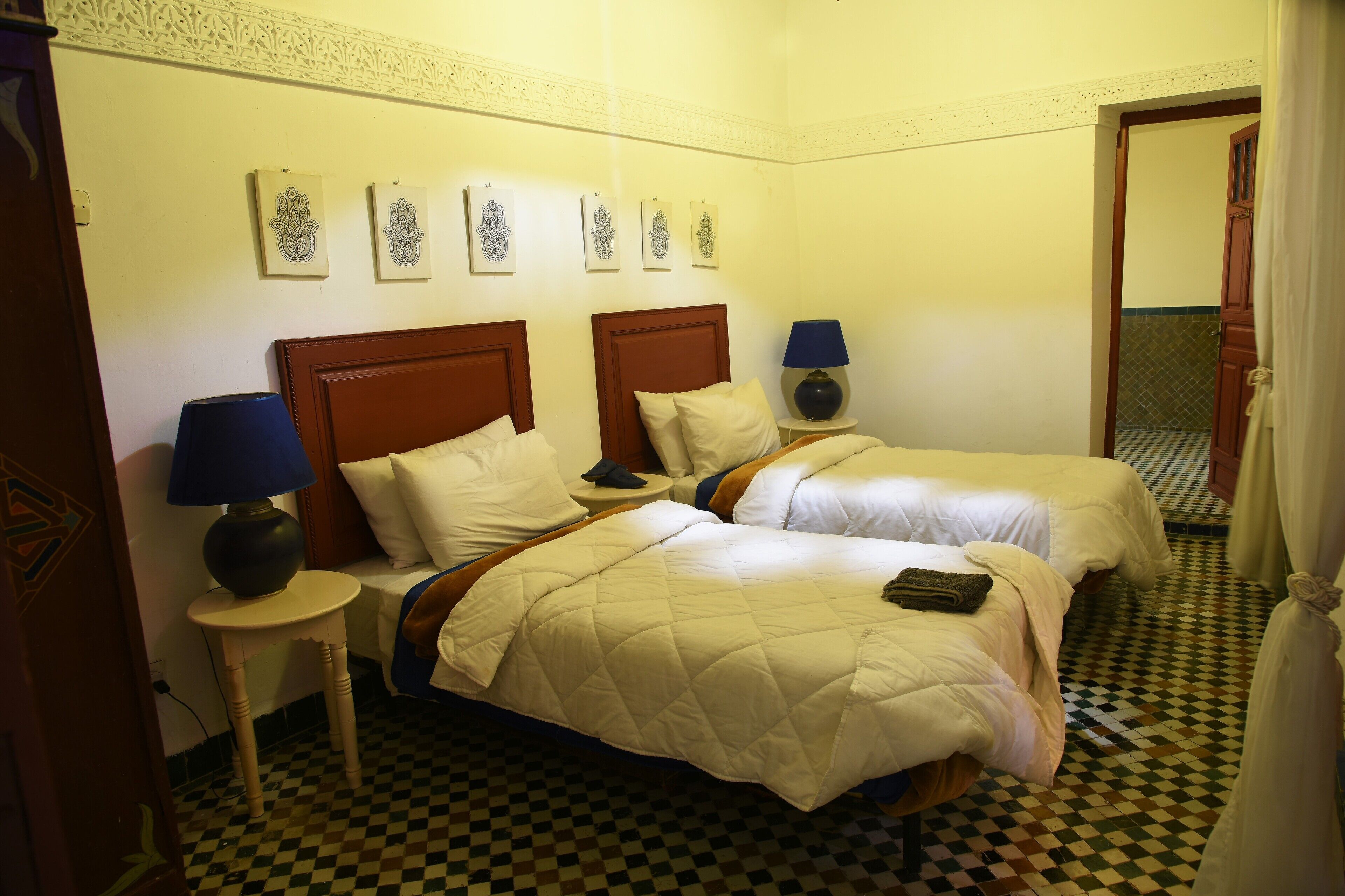 Une chambre d’hôtel avec deux lits, un sol à carreaux et un mur décoratif orné d’œuvres d’art encadrées.