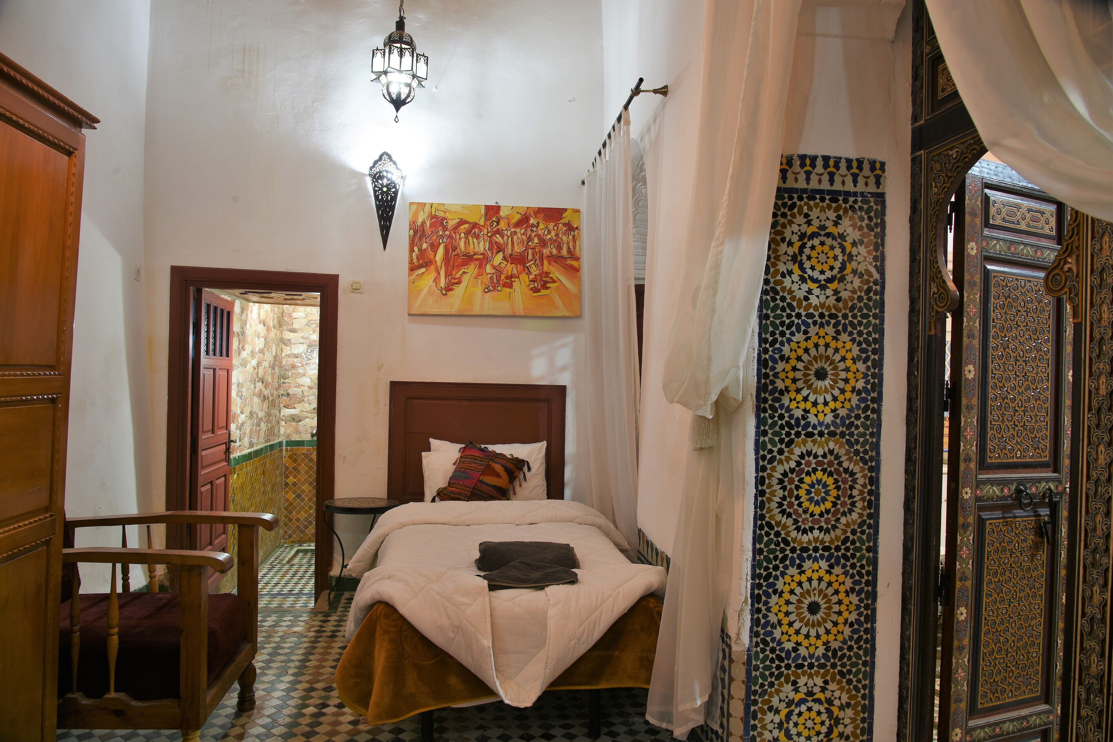 A room with a bed, a wooden chair, a painting, and a patterned wall.