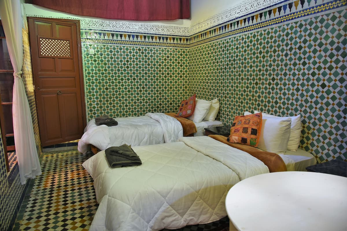 A room with two beds, a small table, and a patterned wall.