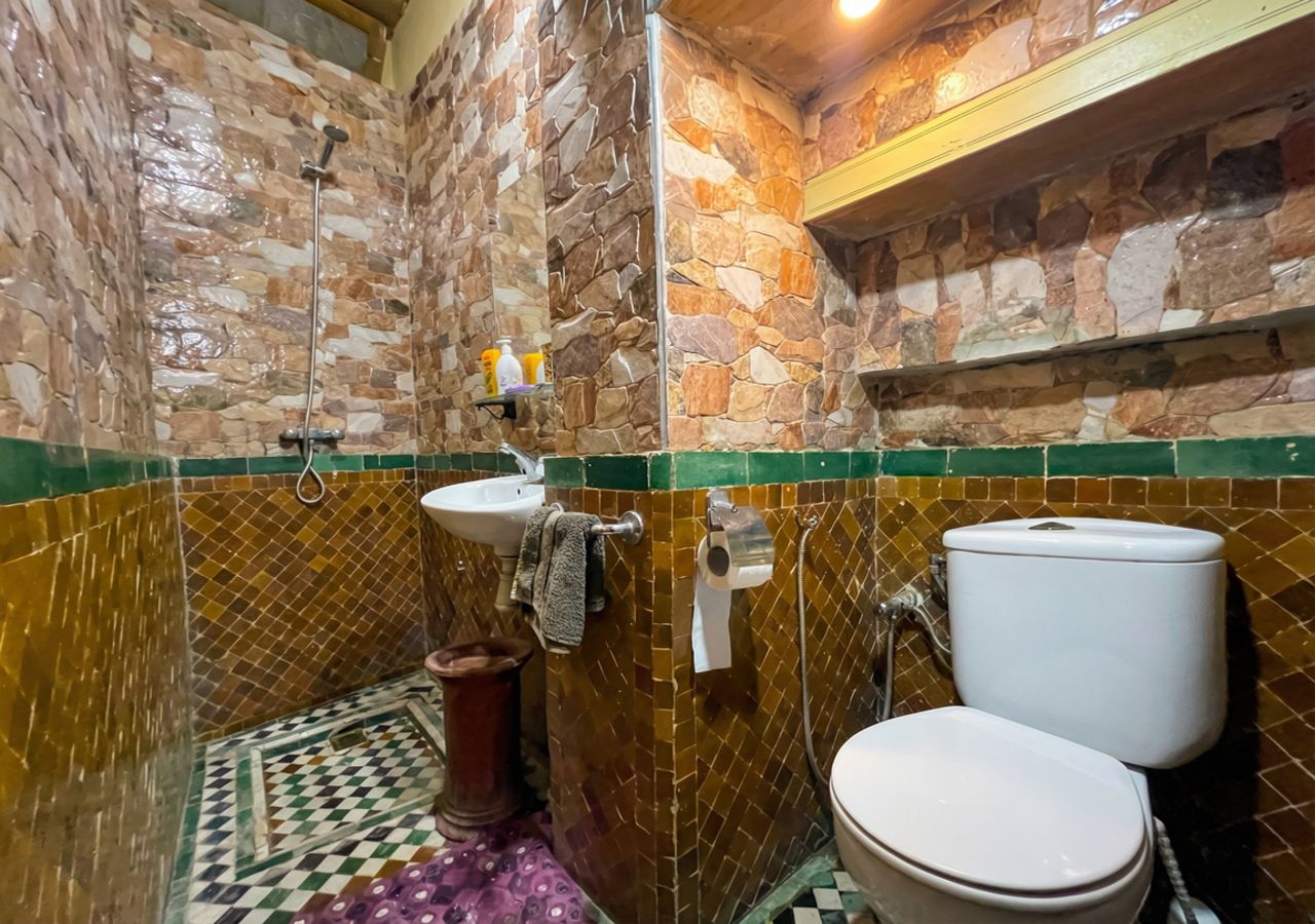 A bathroom with a stone wall, a toilet, a sink, and a shower.