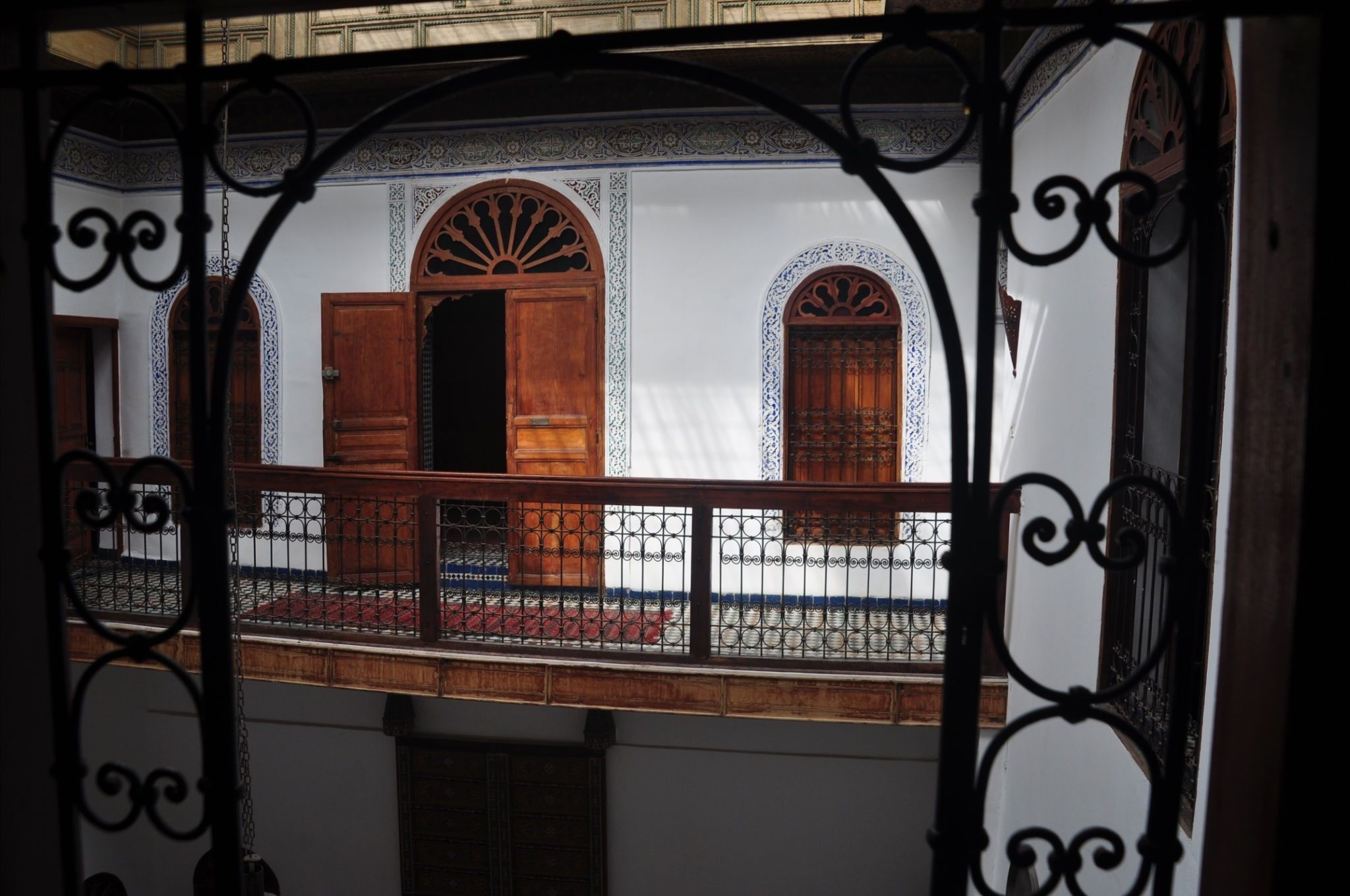 Un balcón con barandillas de hierro forjado decorativas, puertas de madera y baldosas estampadas.
