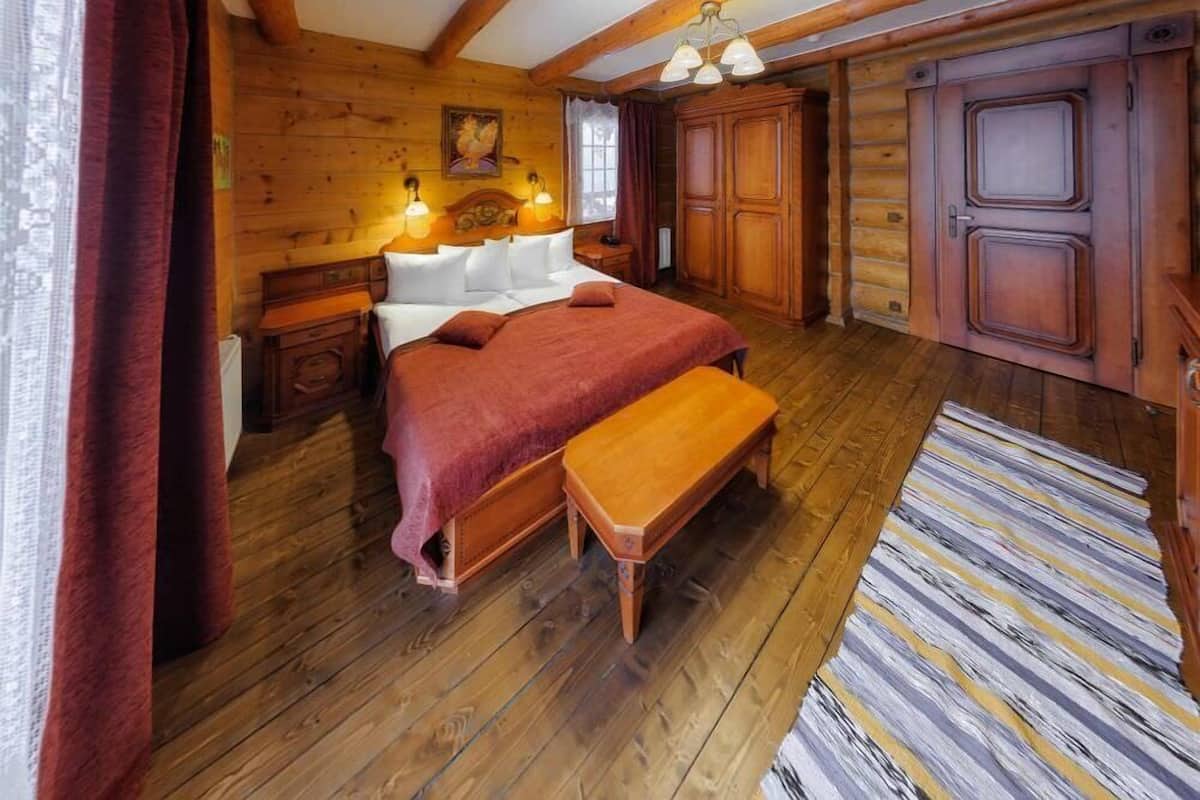 A wooden cabin-style bedroom with a large bed, a bench, a dresser, and a wooden wardrobe.