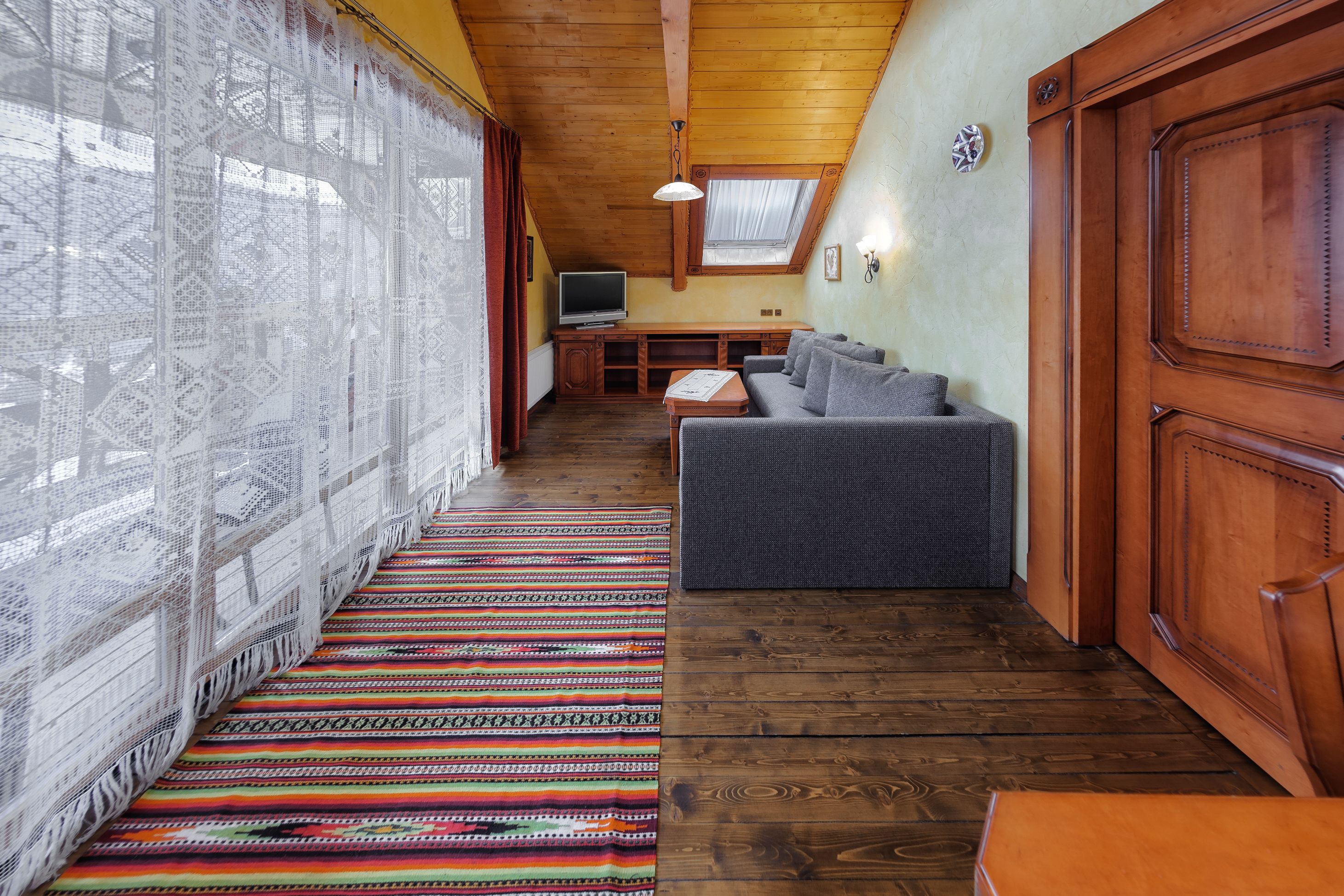 A cozy room with a wooden ceiling, a patterned rug, a gray sofa, and a television.
