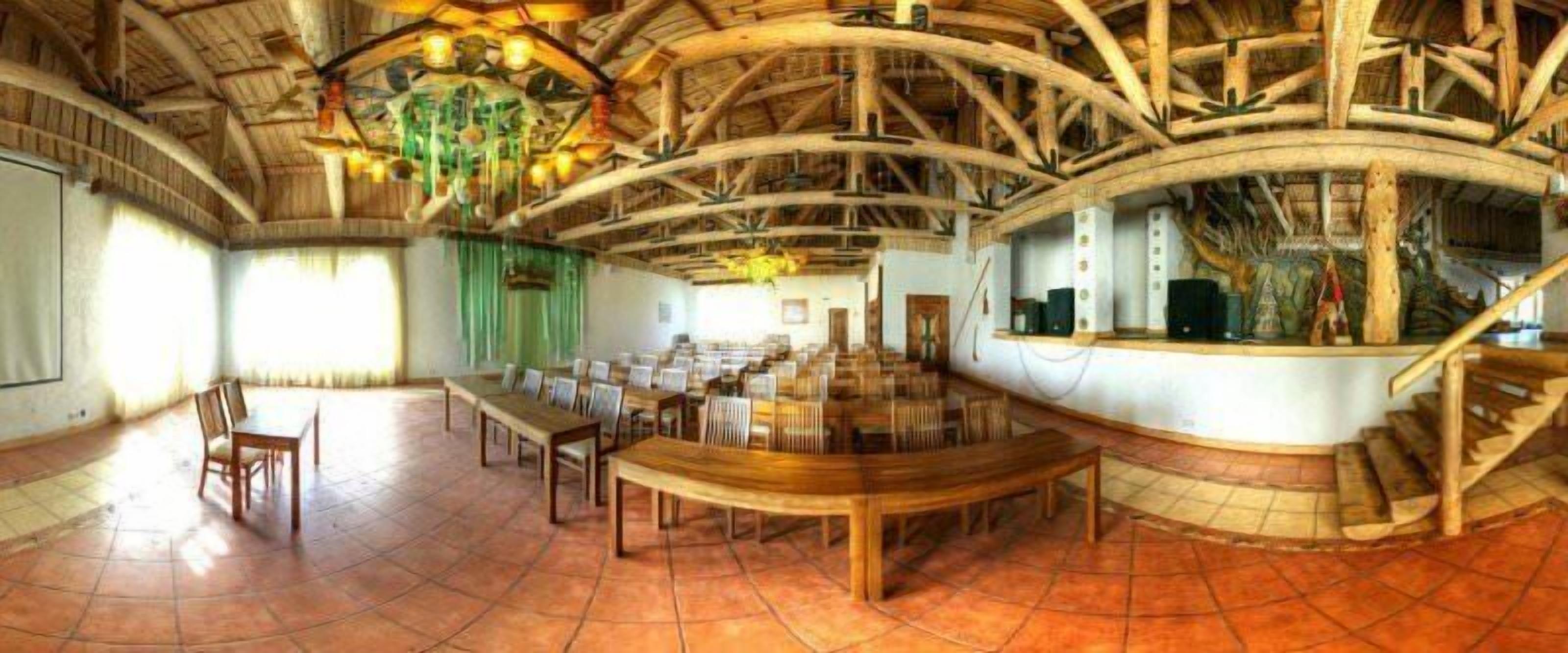 A large hall with a high wooden ceiling, a central table, and chairs arranged around it.