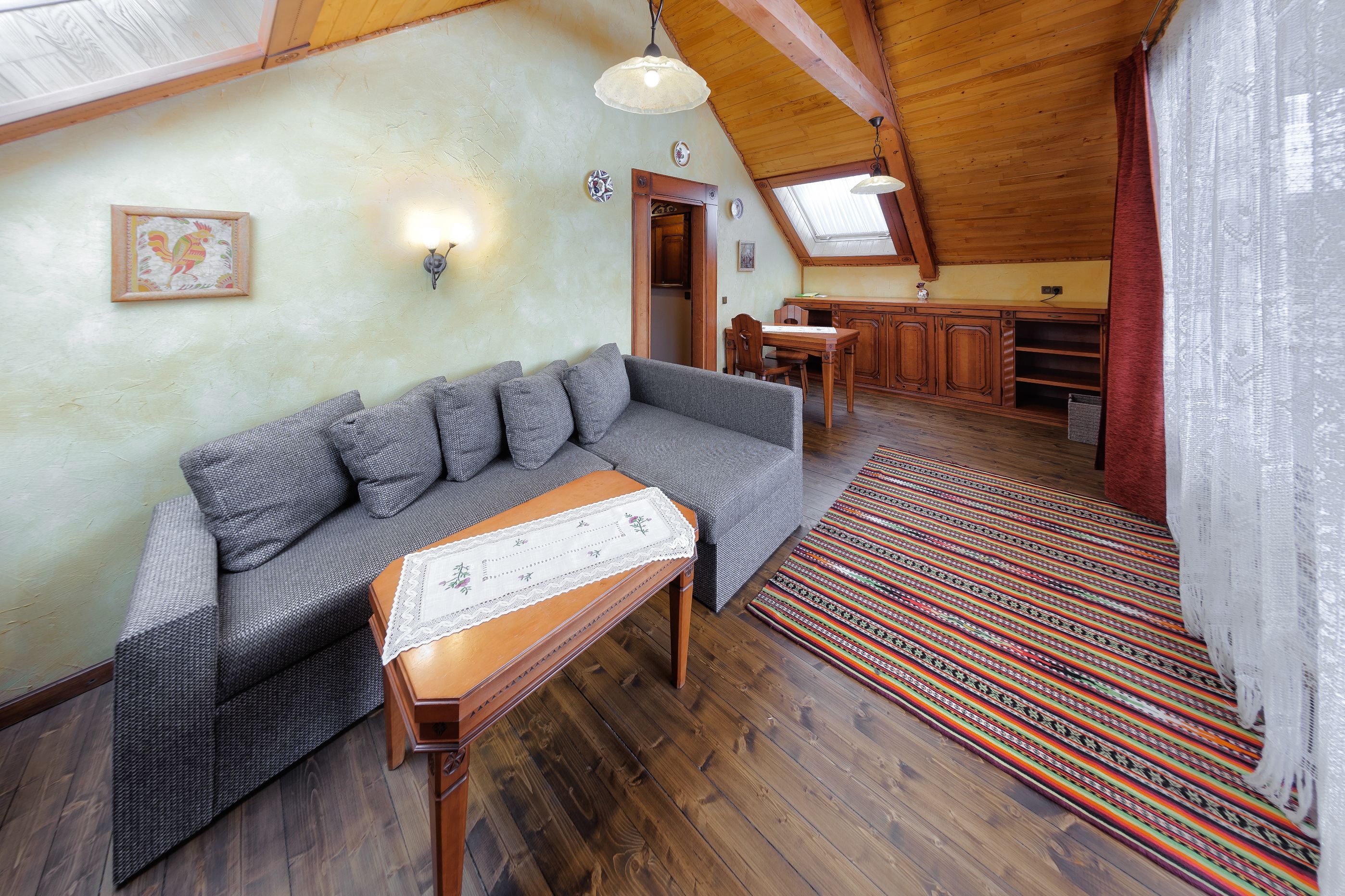 Um quarto aconchegante no estilo loft, com um sofá cinzento, mesa de jantar de madeira e tapete estampado.