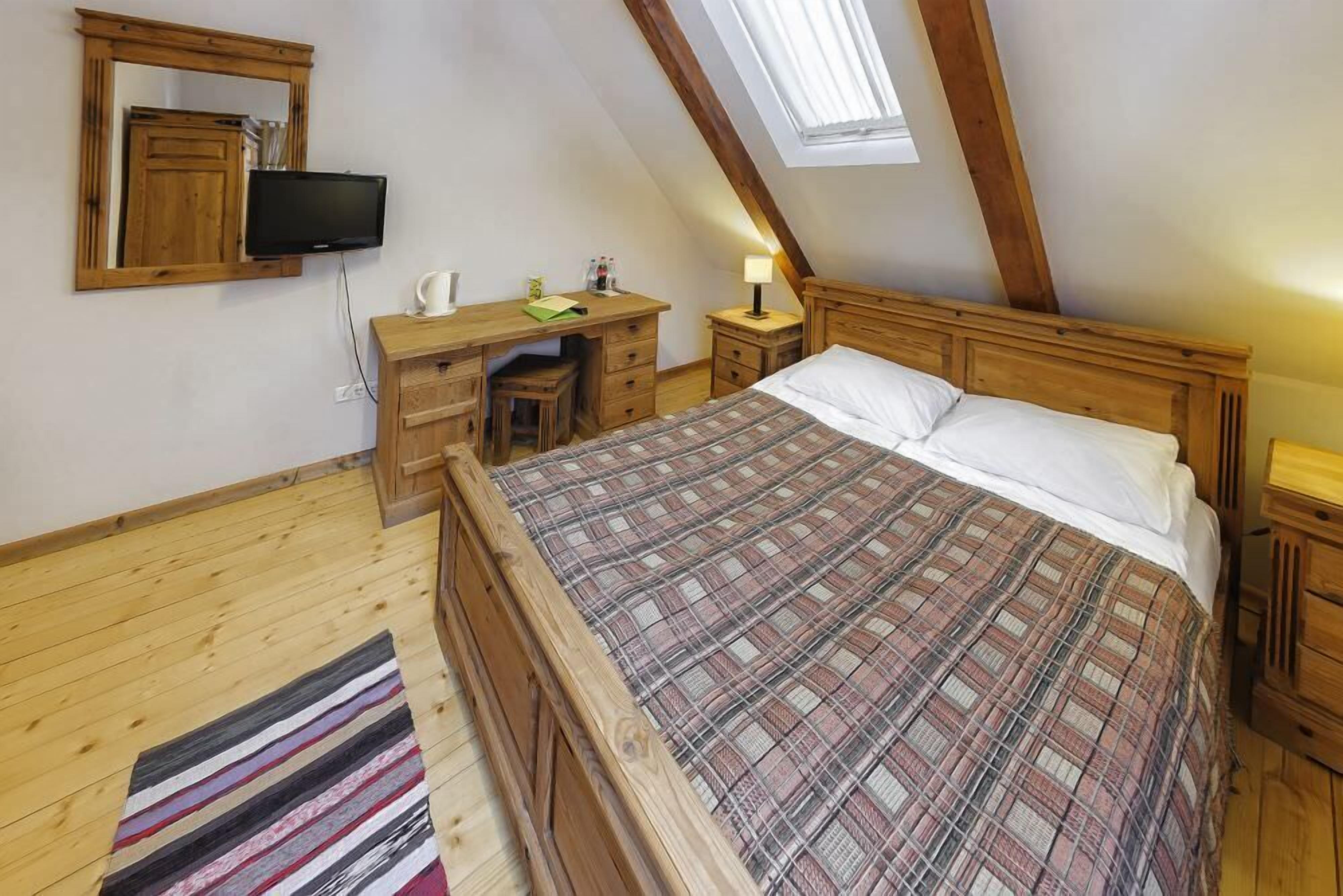 A bedroom with a wooden bed, a desk, a chair, a television, and a skylight.