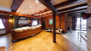A log cabin interior with a wooden floor, a central bench, and a fireplace.