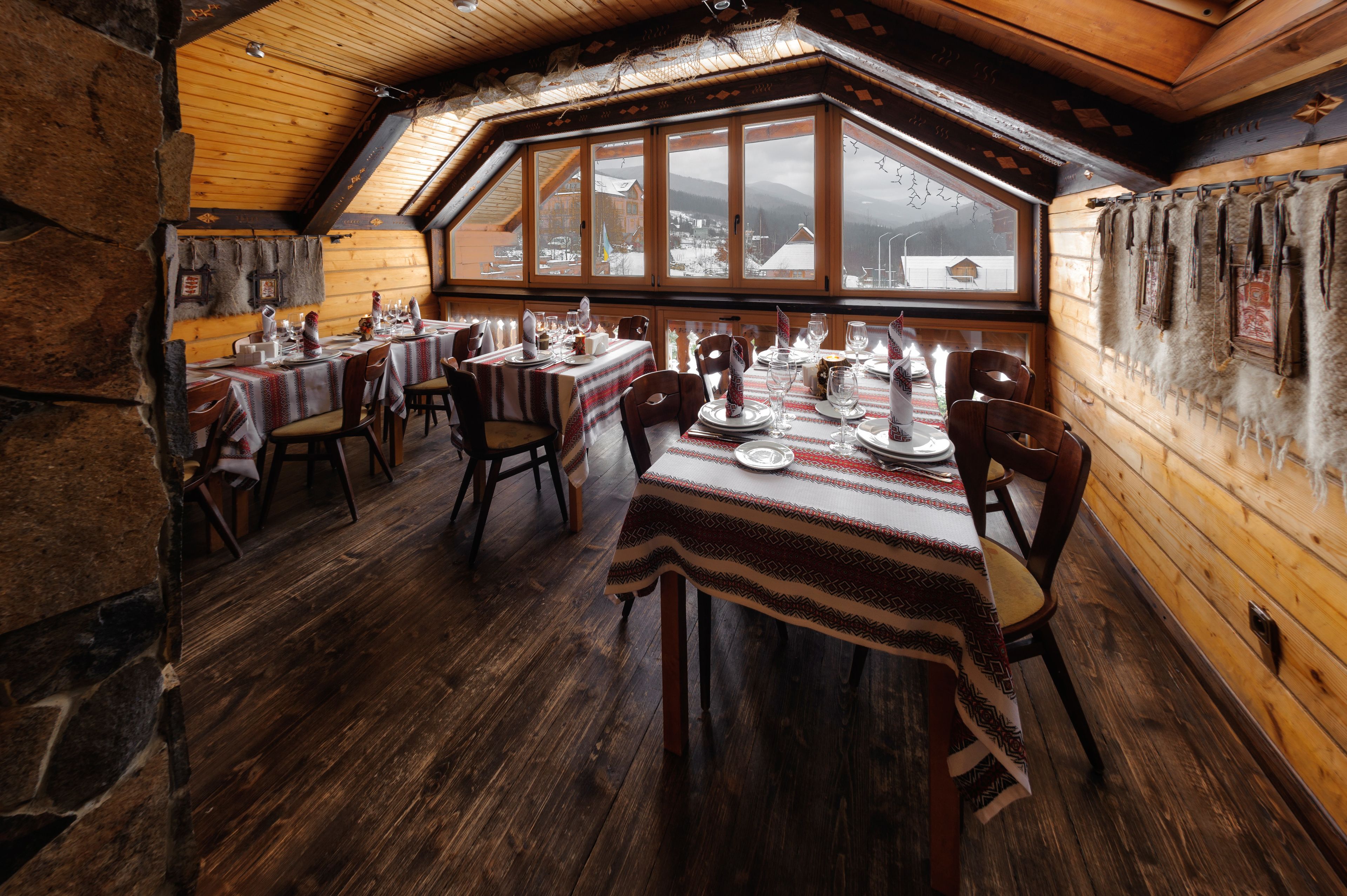 Un restaurant chaleureux aux murs en bois et au plafond incliné, avec des tables dressées pour le dîner, offrant une vue sur un paysage enneigé grâce à de grandes fenêtres.