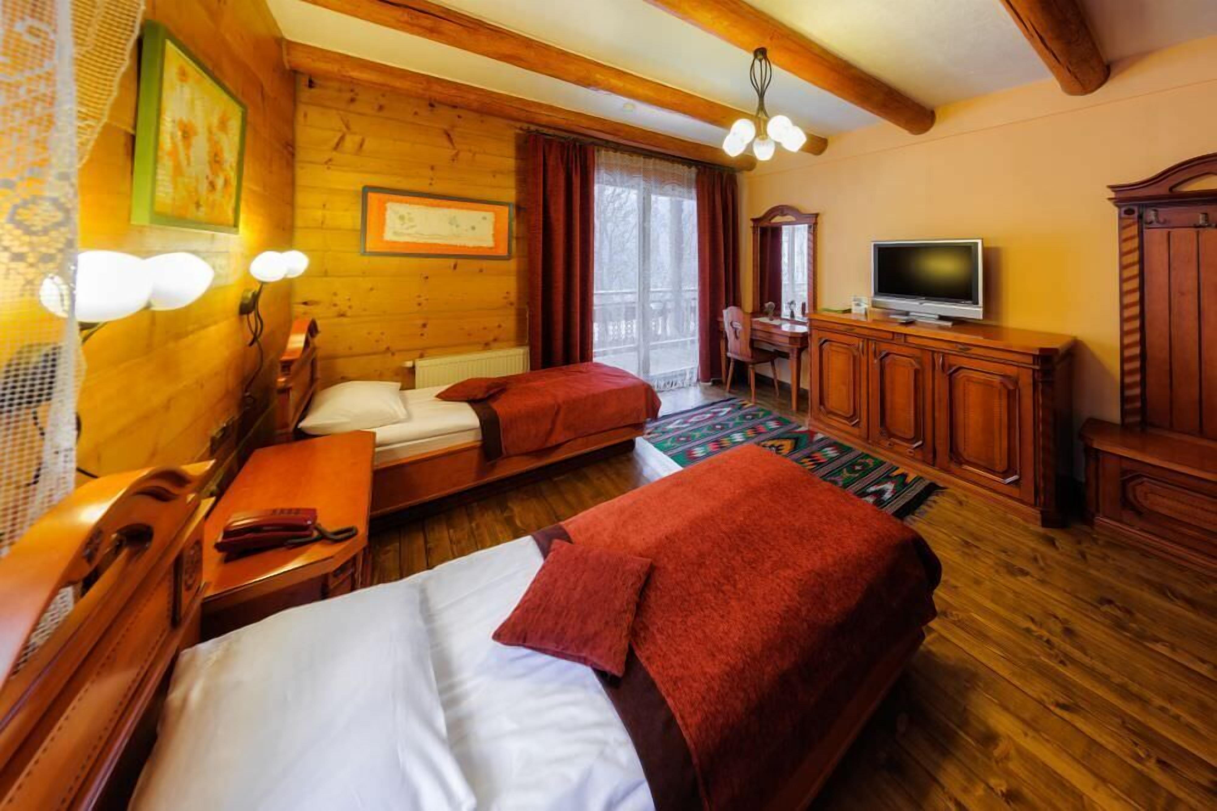 A wooden room with two beds, a TV, a desk, and a mirror.