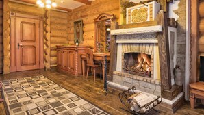 A log cabin interior with a fireplace, wooden furniture, and a patterned rug.