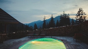A wooden deck with a swimming pool, surrounded by mountains and trees.