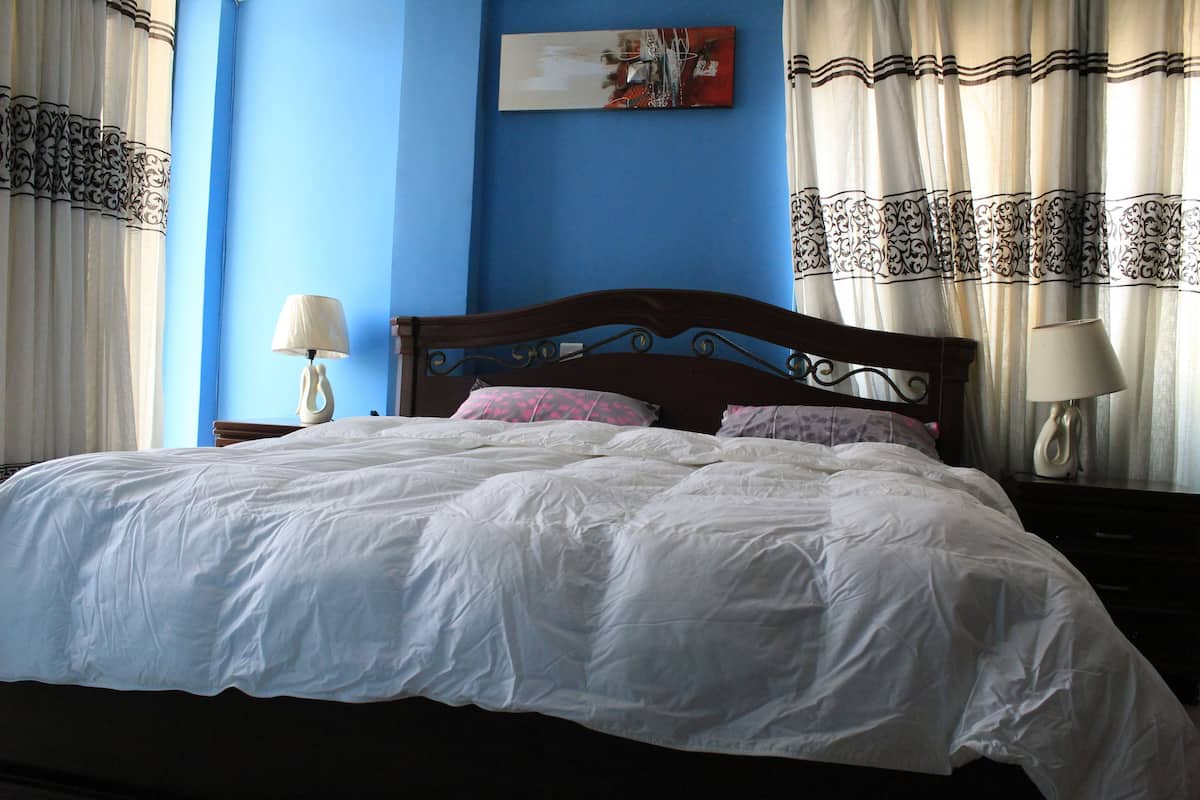 Uma cama bem arrumada com roupa de cama branca, cabeceira de madeira e duas luminárias de cabeceira.
