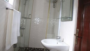 Un baño con cabina de ducha de vidrio, un lavamanos blanco y una puerta de madera.