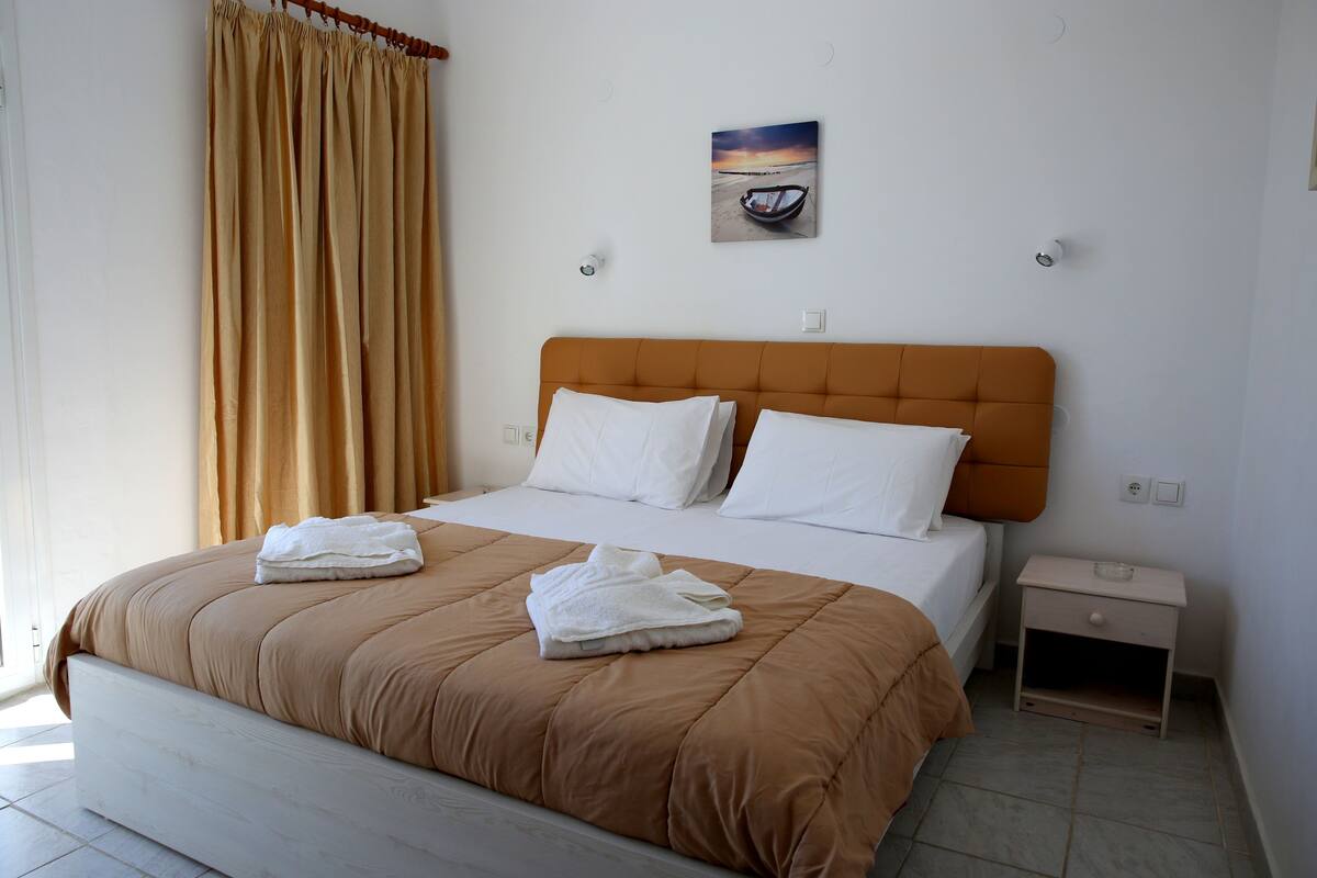 Una cama bien hecha con cabecera marrón, almohadas blancas y toallas dobladas.