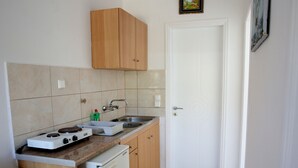 A compact kitchen with a gas stove, sink, and wooden cabinets. - Kappatos Apartments (Kefalonia)
