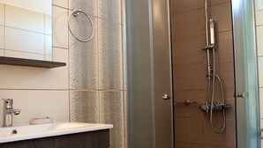 A modern bathroom with a glass-enclosed shower, a vanity with a mirror, and a tiled floor. - Kappatos Apartments (Kefalonia)