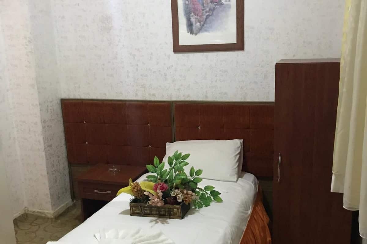 A neatly made bed with a floral arrangement, a wooden headboard, and a wardrobe in a room with patterned wallpaper.