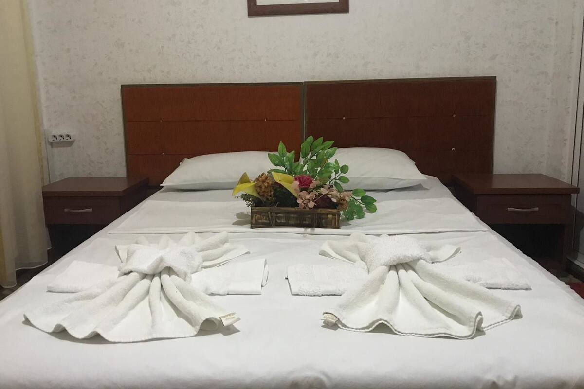 A neatly made bed with white linens, a floral centerpiece, and towels arranged in a fan shape.
