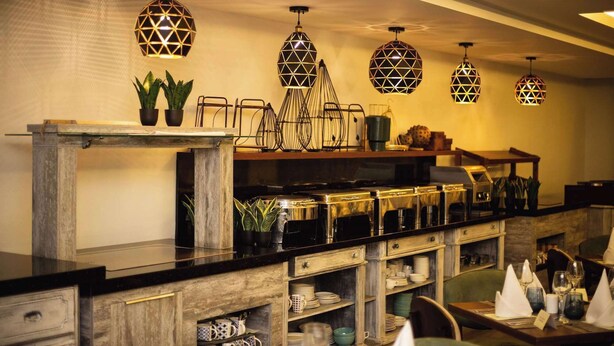 A restaurant interior with a long counter, multiple hanging geometric pendant lights, and shelves with dishes and glasses. - Central Hotel- Ridge (Accra)