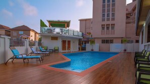 A swimming pool with lounge chairs, a covered area, and a building with balconies. - Central Hotel- Ridge (Accra)