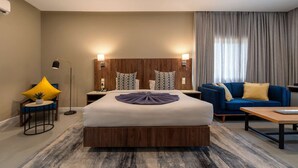 A hotel room with a large bed, a sofa, a coffee table, a lamp, and a nightstand with a phone. - Central Hotel- Ridge (Accra)
