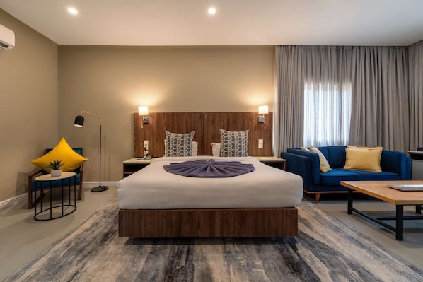 Habitación de hotel con una cama grande, un sofá, una mesita de café, una lámpara y una mesita de noche con teléfono.