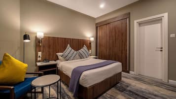 Hotelkamer met een groot bed, nachtkastje, bureau, stoel en een deur.