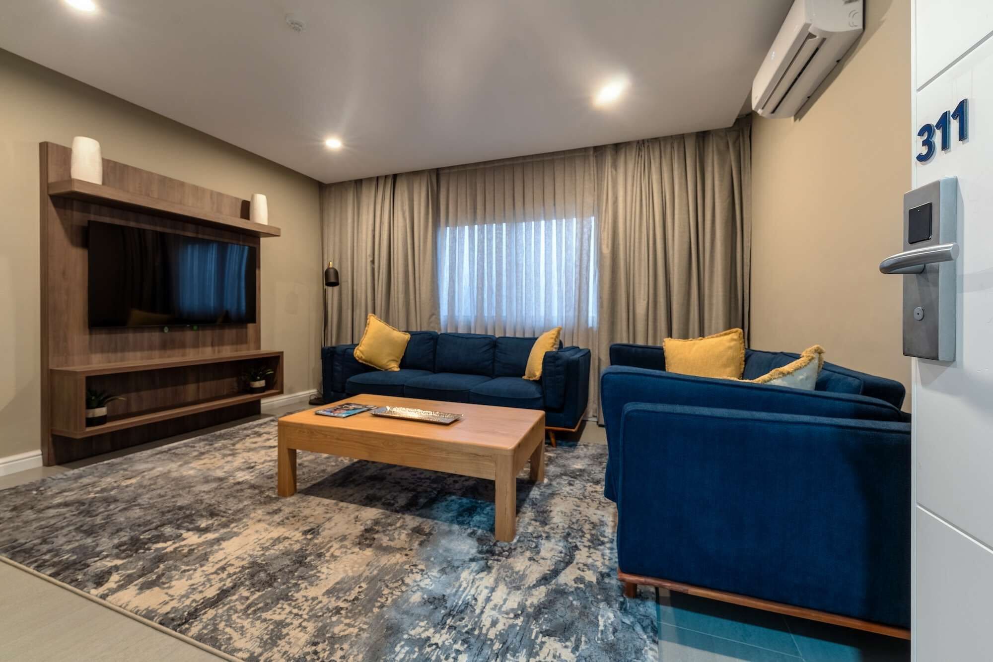 Una sala de estar moderna con un conjunto de sofá, una mesa de centro, un televisor y un amplio ventanal con cortinas.
