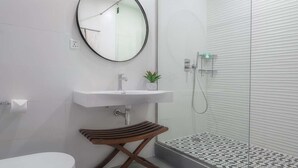 A modern bathroom with a toilet, a round mirror, a sink, and a glass shower enclosure. - Central Hotel- Ridge (Accra)