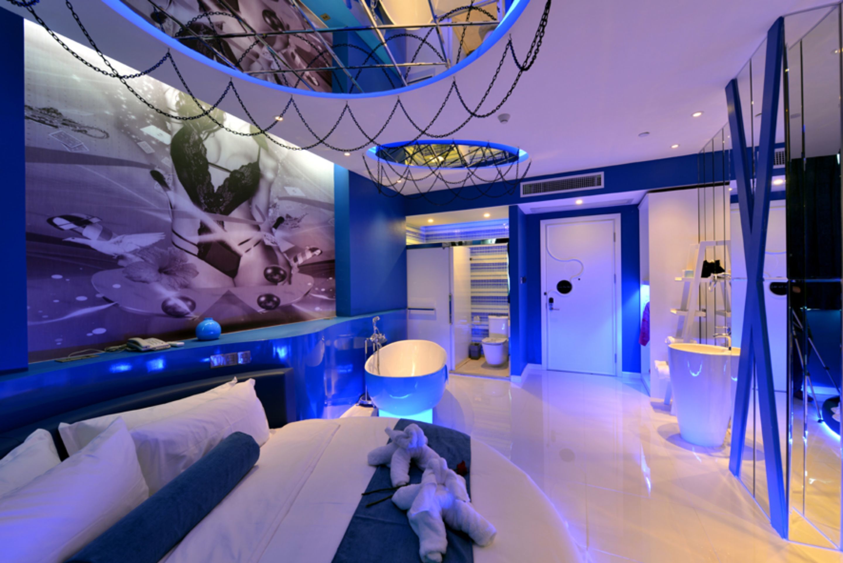 A modern hotel room with a large bed, a decorative wall, a large window, and a bathroom with a white sink.