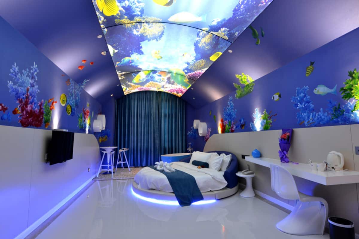 A modern hotel room with a round bed, a desk, and a ceiling aquarium display.