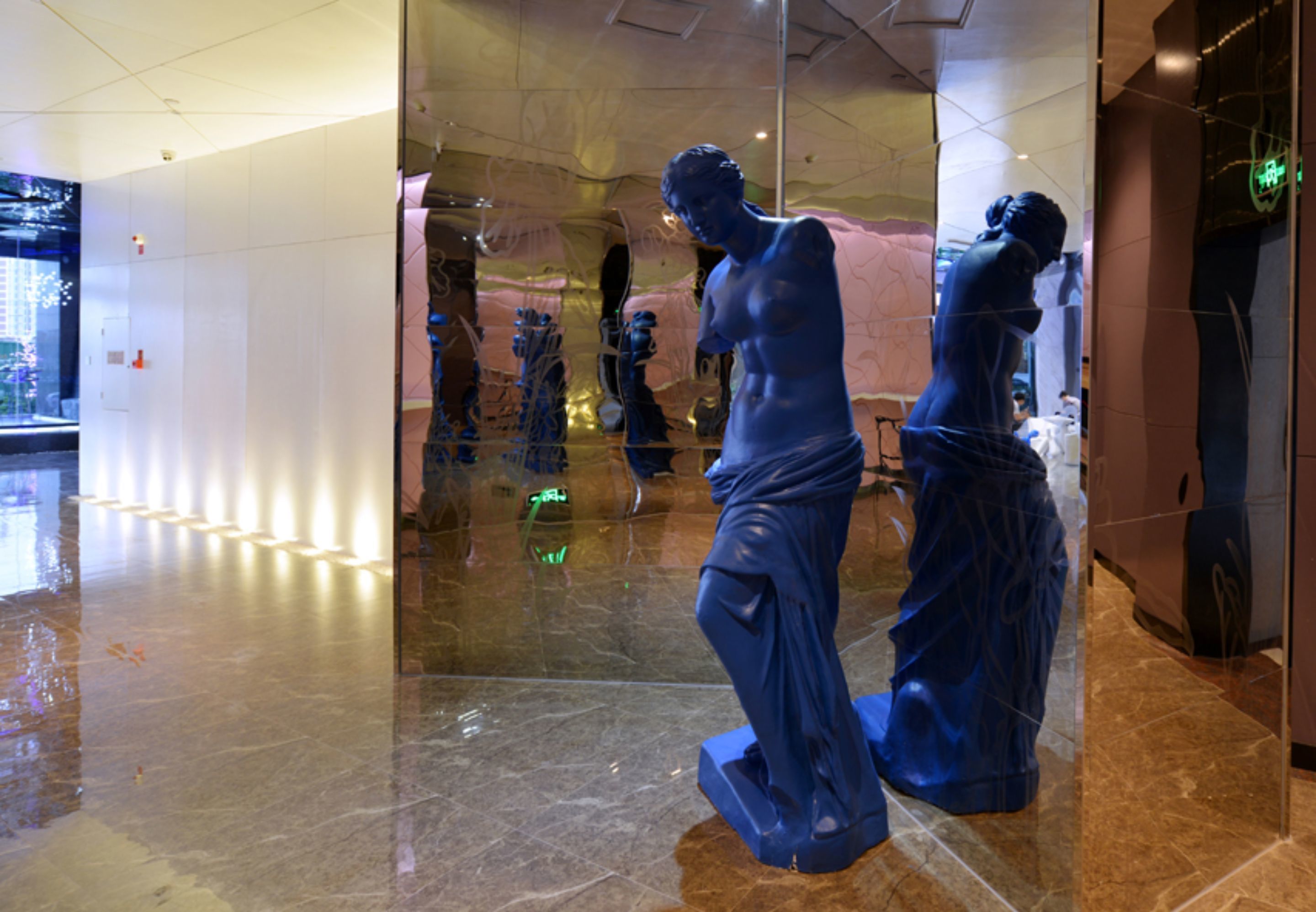 Un intérieur moderne avec des revêtements de sol réfléchissants et des murs en verre, où sont exposées des sculptures.