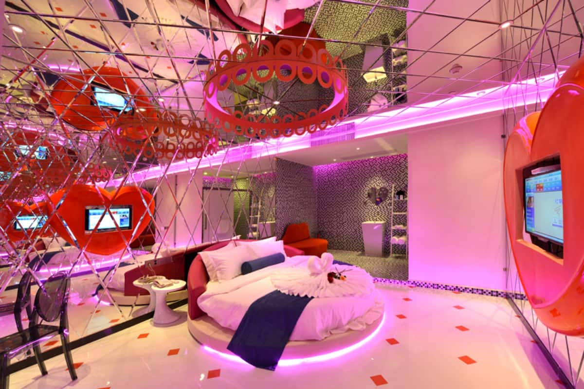 A modern hotel room with a circular bed, a red sofa, and a TV on the wall.