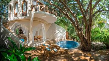 A white, curved building with a pool and outdoor seating area surrounded by trees.
