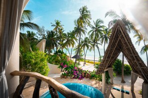 Un área de piscina con una estructura de techo de paja, palmeras y vista a la playa.