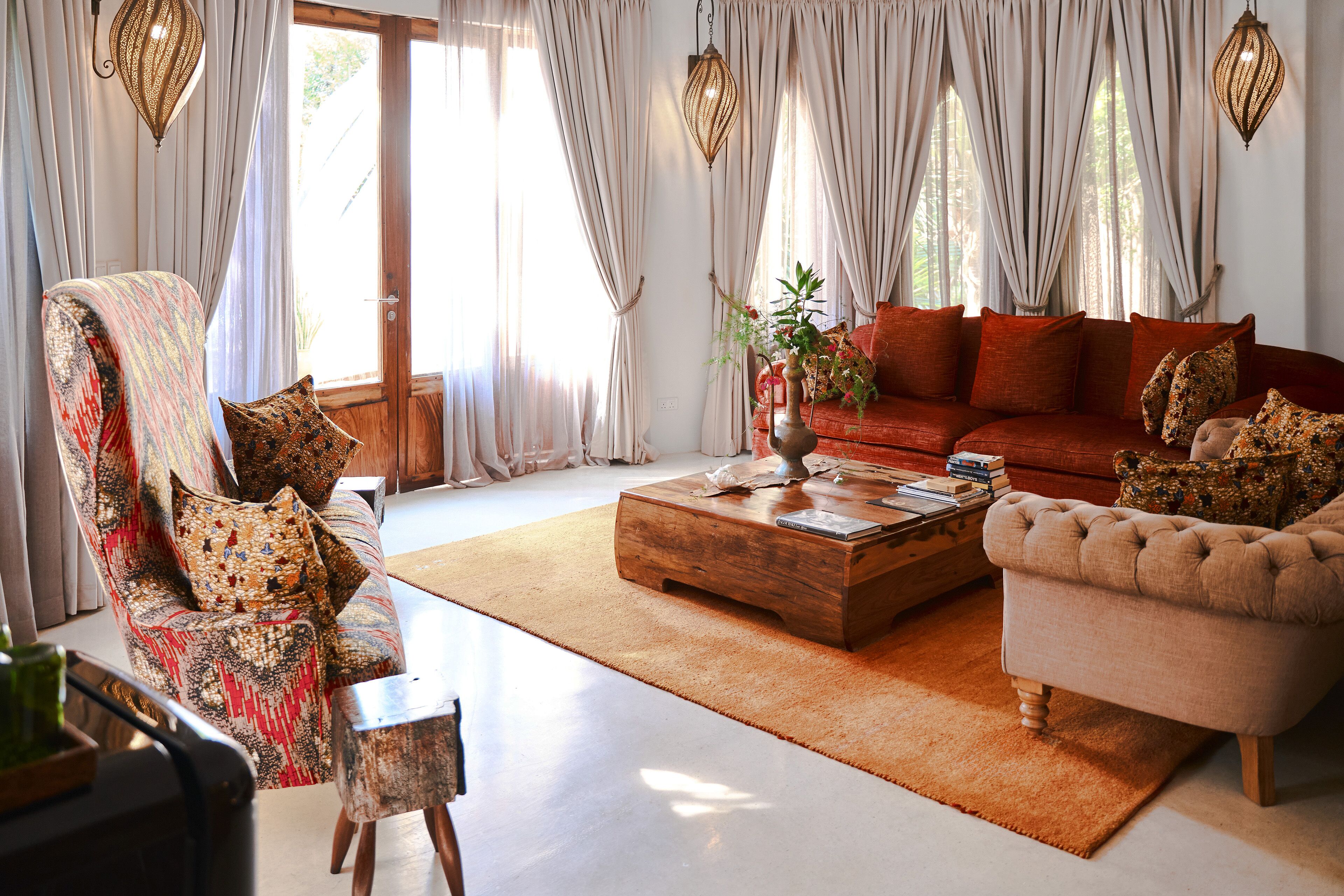 A living room with a sofa, armchair, and coffee table, featuring a large window with curtains and hanging lamps.