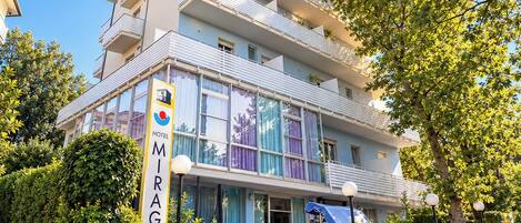 Un hotel de varios pisos con un letrero llamativo, balcones y un jardín bien cuidado.