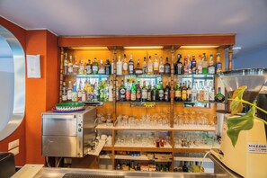 Un espace bar avec des étagères remplies de bouteilles d’alcool, de verres et une machine à café.