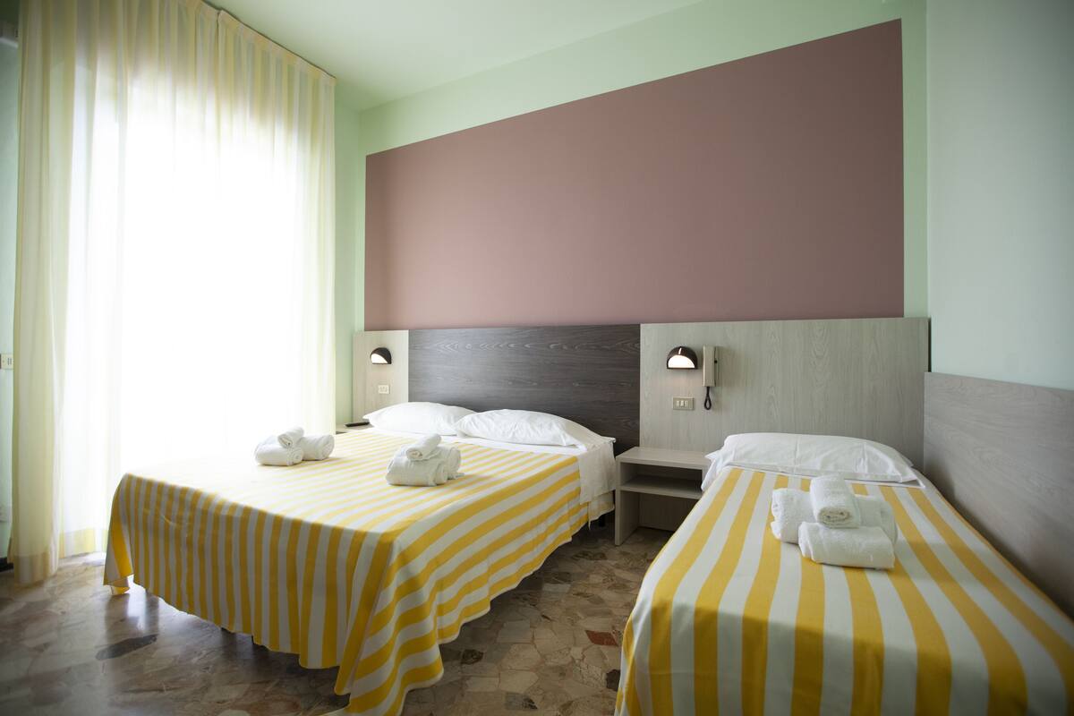 A hotel room with two beds, each with a striped yellow and white bedspread, and a nightstand between them.