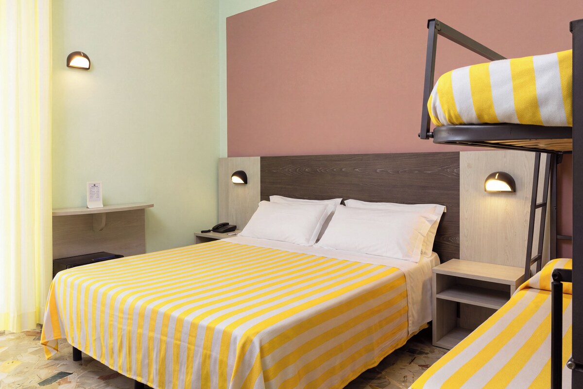 A hotel room with a bunk bed, a bedside table, a lamp, and a bed with striped bedding.