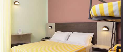 A hotel room with a bunk bed, a bedside table, a lamp, and a bed with striped bedding.