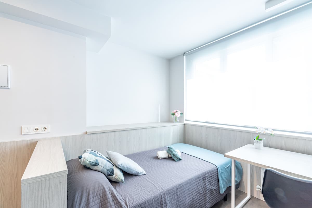 Une chambre moderne et compacte, dotée d’un lit simple, d’un bureau et d’une fenêtre.