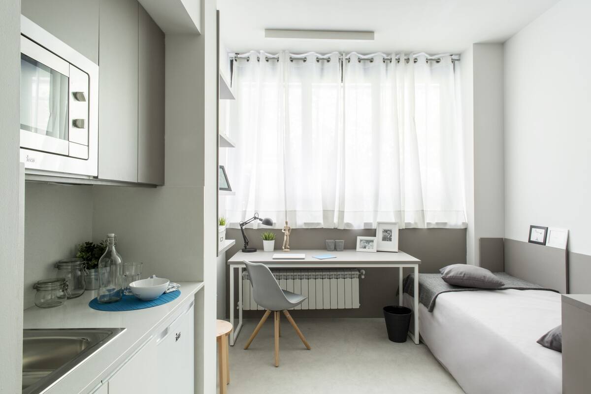 Une chambre à coucher de taille modeste, comprenant un lit, un bureau et une fenêtre avec des rideaux.