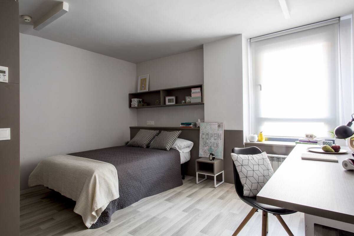 Une chambre moderne comprenant un lit, une table de chevet, une chaise et un bureau avec une lampe.