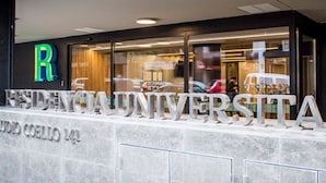 L’entrée d’un bâtiment universitaire, avec une grande enseigne indiquant « RESIDENTIA UNIVERSITARIA » et, à droite, une autre enseigne avec l’inscription « ON MANGER » !