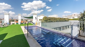 Une piscine sur le toit offrant une vue dégagée sur les gratte-ciel de la ville, entourée de verdure et d’une architecture moderne.