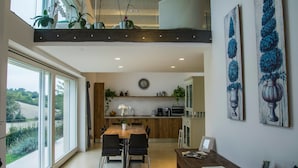 Cocina moderna con armarios de madera, un comedor con mesa y sillas de madera, y vistas al exterior a través de amplias ventanas.