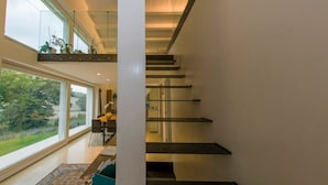 Un interior moderno con una escalera, ventanas amplias y vistas al exterior con vegetación.